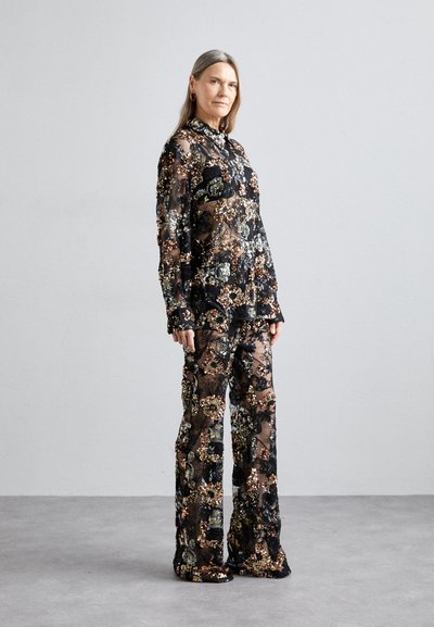 Ensemble noir transparent avec des motifs floraux, comprenant un haut à col et manches longues, ainsi que des pantalons évasés, ornés de sequins colorés et de broderies.
