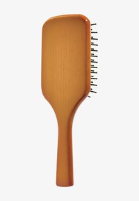 Harjattu puinen hiusharja suorakaiteen muotoisella lätkällä, sileällä oranssinkellertävällä pinnalla ja mustilla metalliharjaksilla, jotka ovat tasaisesti sijoitettu laitamille.