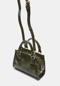 Zelena torbica iz umetne kože s teksturiranim mrežastim vzorcem, zgornjima ročajema in nastavljivim ramenskim trakom. Ima zlate kovinske dele in zadrgo.