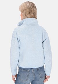 Heled sinine fleece-jakke kõrge kraega, tekstureeritud kangast ja raglanvarrukatega. Omab lühendatud disaini ja kontrastset ääreviimistlust alläärtes.