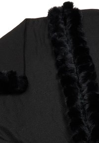 Schwarzes Kleidungsstück aus strukturiertem Stoff mit einem plüschigen, fellartigen Kragen und Besatz. Das Design umfasst eine offene Vorderseite und eckige Revers.