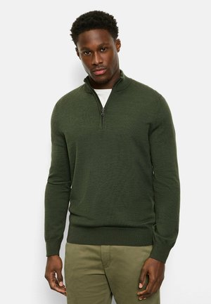 Grüner Pullover mit Viertelreißverschluss aus strukturiertem Strickstoff, mit hohem Kragen und gerippten Bündchen, getragen über einem weißen Hemd.