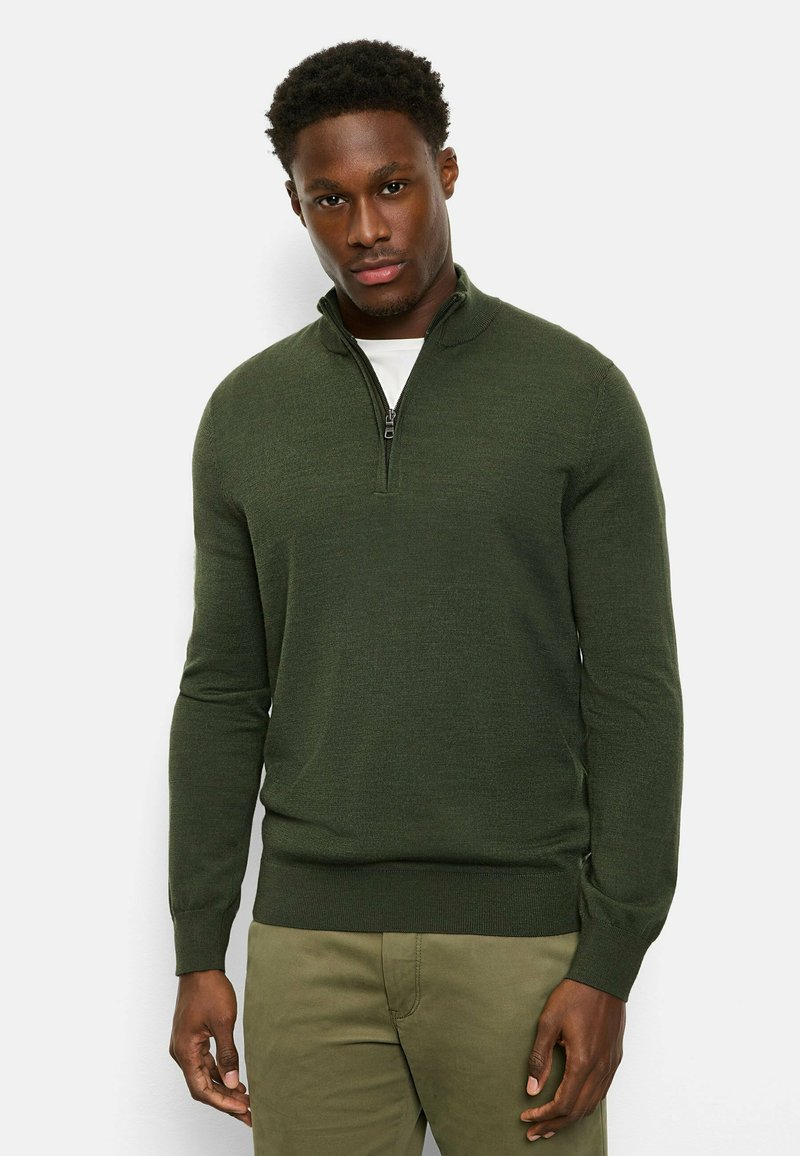Green quarter-zip sweater made of textured knit fabric, featuring a high collar and ribbed cuffs, worn over a white shirt.
