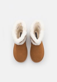 Bottines en daim marron avec doublure en shearling blanc duveteux visible au niveau du col, vues de dessus sur un fond blanc.