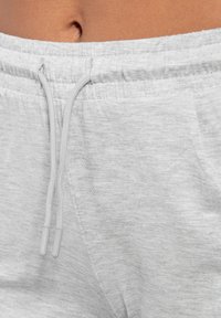 Pantaloni da jogging in cotone grigio chiaro con vita elasticizzata. Presentano un cordoncino con punte grigie e tasche laterali. Tessuto morbido, design casual.