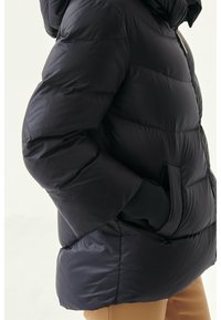 Mustapuffatakki hupparilla, jossa on vuoratut osat, vetoketjukiinnitys ja sivutaskut. Materiaalissa on kiiltävä pinta.