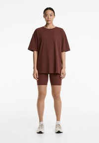 Bordeaux oversized t-shirt met korte mouwen, gecombineerd met bijpassende strakke shorts. De stof lijkt zacht, met een gladde textuur. Witte sneakers maken de look compleet.