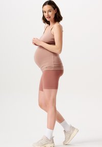 Graviditetsoutfit med en lysebrun, tætsiddende tanktop og matchende ribbede cykelsHORTS. Modellen bærer lyse sneakers og hvide strømper.