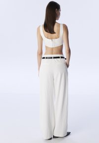 Witte textuur crop top met een vierkante rits aan de achterkant, gecombineerd met high-waisted, wijde broek met een zwarte accentriem.
