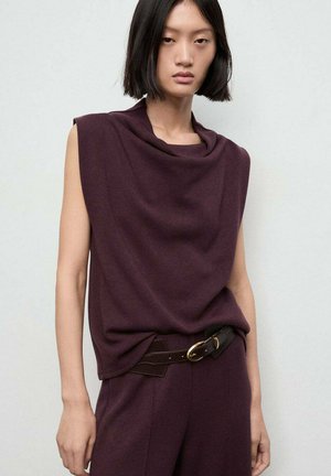 Woman with straight black hair wears sleeveless dark purple top and matching pants with a black belt featuring a gold buckle.