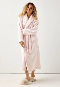 Lyserød fleecebadekåbe med lange ærmer, slå-om-design, sidelommer og bælte. Blød tekstur og knælængde. Brugt sammen med bløde tøfler.