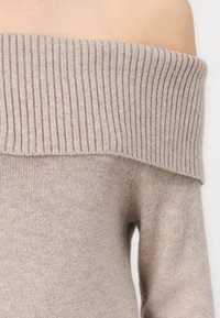 Μπεζ πουλόβερ εκτός ώμου φτιαγμένο από μαλακό, υφαντό ύφασμα με φαρδύ ριμπ μανίκι και εφαρμοστές μαν sleeves. Ελαφρώς πλεκτές λεπτομέρειες σε όλη την επιφάνεια.