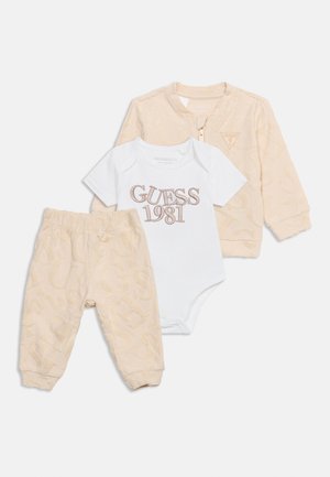 Beige babyjasje en broek met alfabettextuur, gecombineerd met een witte korte mouw body met de tekst "GUESS 1981" in bruine letters.