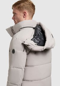 Giacca a vento grigio chiaro con collo alto, design trapuntato e fodera interna nera. Presenta tasche con zip e un patch con logo.