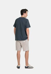 Dark gray cotton t-shirt with short sleeves, paired with light beige corduroy shorts. Model shown from the back, wearing dark athletic shoes.