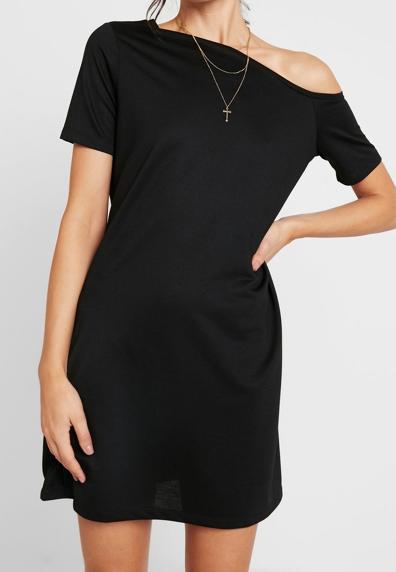 Černé šaty s odhalenými rameny a krátkými rukávy, vyrobené z měkké tkaniny. Mají uvolněný střih a mírnou křivku na lemu. Zlatý vrstvený náhrdelník.