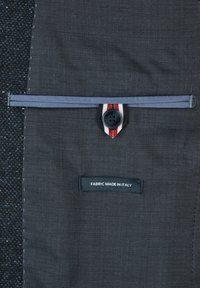 Dunkelgrauer Stoff mit einem dezenten Muster, ausgestattet mit einem Knopfverschluss und einem Etikett, auf dem steht "STOFF AUS ITALIEN". Enthält ein kontrastierendes Streifendetail.