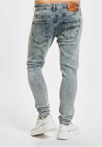Lyseblå denimjeans med falmet finish, smal passform og to baklommer. Festet skinnlapp ved midjebåndet. Brukes med hvite joggesko.