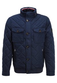 Marinblå quiltad jacka med hög krage, två bröstfickor och två sidofickor med dragkedja. Har bruna knappar samt ribbade ärmslut och nederkant.