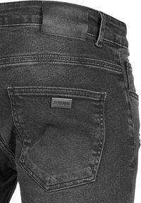 Jeans de mezclilla negra con una textura suave, un bolsillo trasero con una etiqueta de marca y una cinturilla resistente con detalles de logo en relieve.