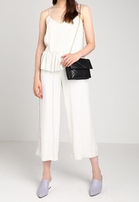 Top peplum bianco a righe sottili abbinato a pantaloni larghi bianchi. Una borsa nera trapuntata e mule lavanda completano il look.