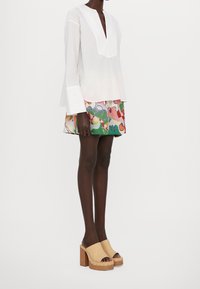 Blouse à rayures blanches avec un décolleté profond en V et des manches larges, associée à une mini-jupe à motifs colorés et des sabots beiges à plateforme.