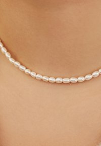Collier en perles avec des perles blanches en forme ovale, texture lisse et taille uniforme, reposant sur une peau nue.