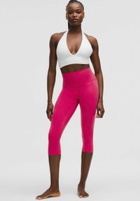 White halter sports bra paired with high-waisted, capri-length leggings in a vibrant pink hue, featuring smooth, stretchy fabric.