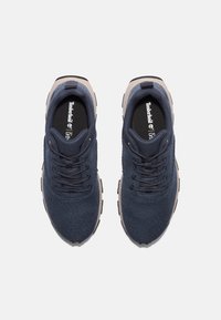 Marineblaue Sneakers mit einem strukturierten Mesh-Obermaterial, flachen Schnürsenkeln, gepolstertem Kragen und beigen Akzenten an der Sohle und Ferse. Timberland-Logo sichtbar im Inneren.