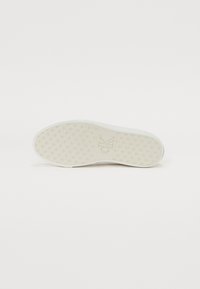 Semelle de sneaker blanche avec une texture et un motif de grip. Présente un logo 'CK' en relief au centre. Design simple et minimal.