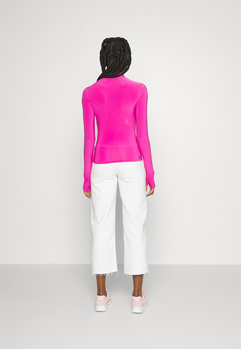 Haut ajusté à manches longues en tissu rose vif, associé à un pantalon cropped blanc, affichant une texture lisse et un design simple, avec un matériel minimal.
