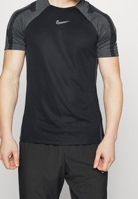 Camiseta deportiva negra de manga corta, con detalles texturizados en gris en los hombros y un logo blanco de Nike en el pecho. Tejido suave.