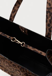 Saco tote com padrão de leopardo castanho, textura de camurça, interior preto, alças duplas e um fecho em tom dourado numa alça interior.