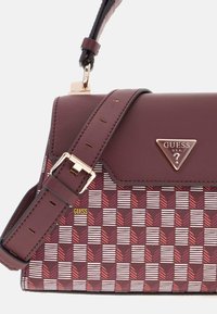 Red and white patterned handbag with a maroon leather flap, gold hardware, and an adjustable strap. Features a logo tag on the front.