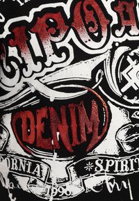 Schwarzer Stoff mit weißem und metallisch rotem Grafikdruck. Enthält verschiedene Beschriftungen und Designs, darunter "DENIM" in fettem, strukturiertem Rot.