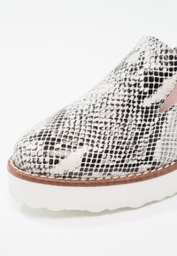 Chaussure à enfiler avec un dessus en imprimé serpent noir et blanc, une texture lisse, une semelle plate blanche et un design à bout arrondi.