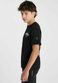 T-shirt en coton noir à manches courtes, avec impression du logo à l'avant et un patch carré sur la manche gauche. Coupe droite avec une coupe classique.