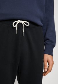 Czarne spodnie dresowe ze białym sznurkiem zakończonym srebrnymi końcówkami, w zestawie z granatową bluzką z długim rękawem. Miękki, casualowy materiał, luźny krój.
