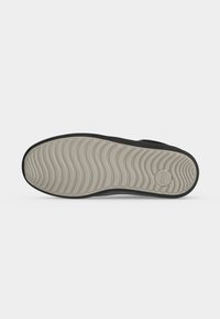 Suela de zapato con patrón de dibujo ondulado gris claro y un logo circular cerca del talón, sobre un fondo blanco liso.