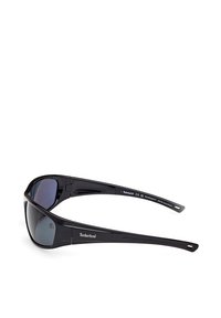 Gafas de sol negras con un acabado brillante, diseño envolvente, lentes reflectantes y la marca Timberland en el costado de la montura.