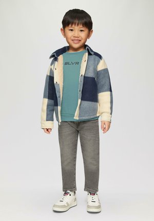 Kind trägt eine navy- und cremefarbene karierte Fleecejacke über einem türkisfarbenen Sweatshirt mit dem Aufdruck "SLVR". Graue Jeans und weiße Sneakers runden das Outfit ab.