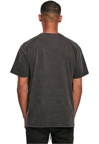 Sort bomulds t-shirt med korte ærmer og en afslappet pasform, synlige syninger og en let falmet tekstur. Bagfra viser den et enkelt design.