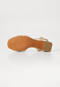 Sandalia beige con suela de madera, tacón cuadrado y correas ajustables. La suela presenta un acabado texturizado para mayor agarre.
