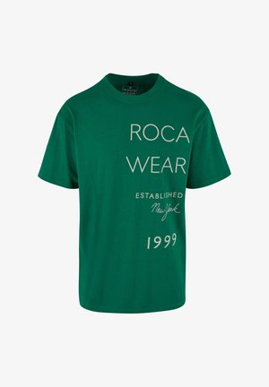 Grøn bomulds t-shirt med rund hals; har "ROCA WEAR" i store bogstaver og mindre tekst der siger "ETABLERT New York 1999."