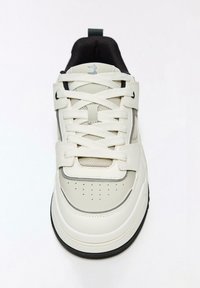 Fehér és szürke tornacipő sima bőr felsőrésszel, hálós részletekkel, lyukacsos orr-résszel, fekete gumitalppal és lapos fűzőkkel.