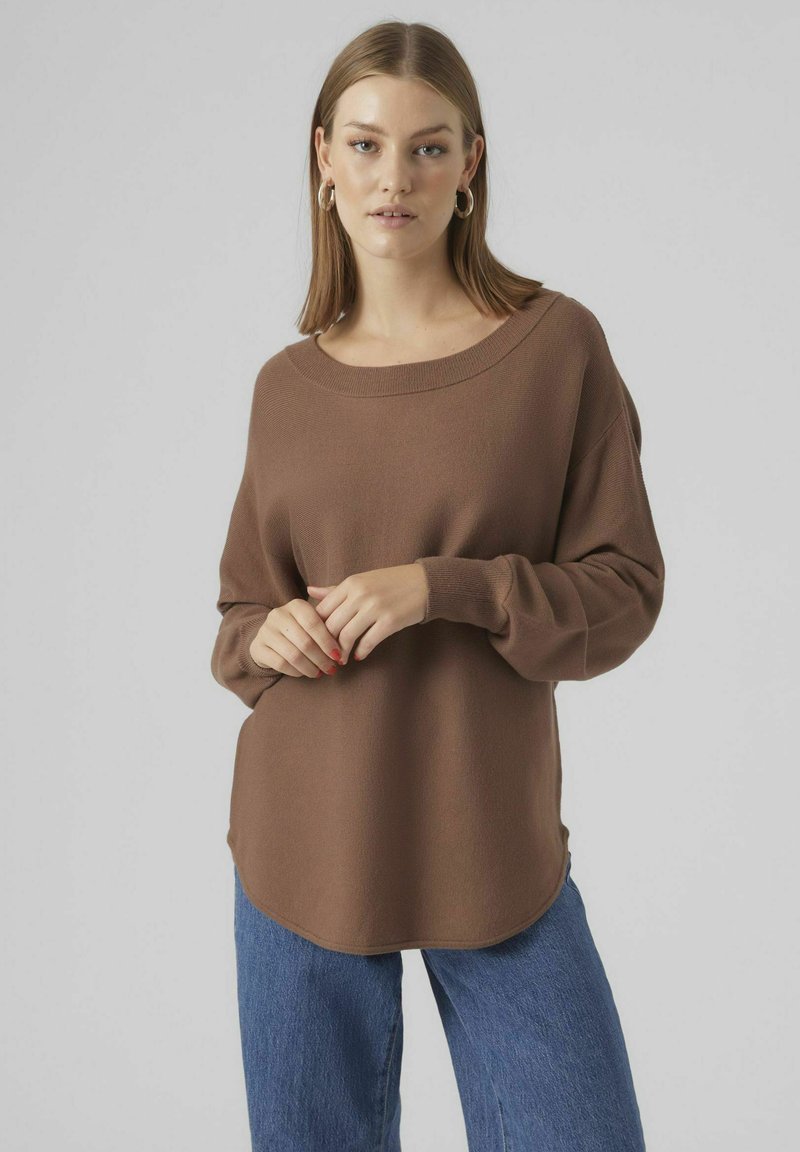 Maglione marrone a maniche lunghe con scollo ampio e vestibilità rilassata, abbinato a jeans blu a gamba larga. Texture morbida, design minimale e senza motivi visibili.