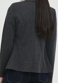 Mörkgrå stickad blazer med figursydd design, enkel ryggslits och långa ärmar. Har en subtil textur och en mjuk yta.