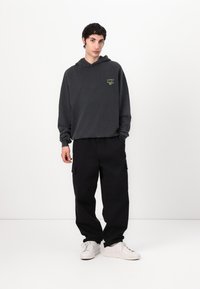 Gray hooded sweatshirt with green graphic on the chest, paired with black cargo pants and white sneakers. Relaxed fit and soft texture.