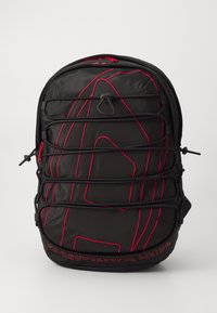Sac à dos en nylon noir avec des coutures rouges accentuées, une surface texturée et des bretelles ajustables. Un texte brodé en bas indique : "POUR UNE VIE RÉUSSIE."