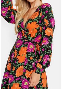 Robe fleurie avec un décolleté en V profond, ornée de fleurs vibrantes orange et violettes sur fond noir, manches longues bouffantes et ceinture à nouer.